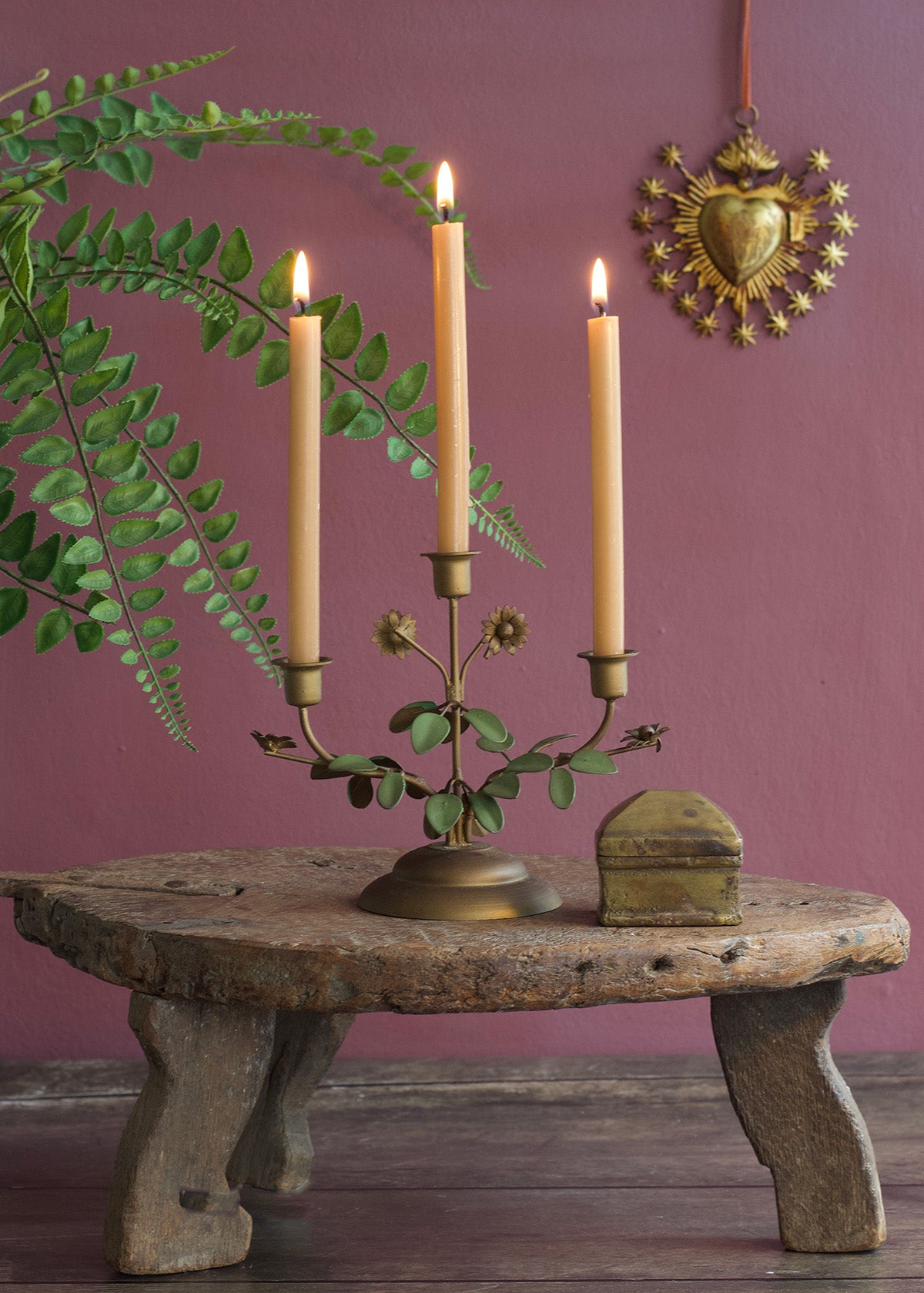 Candle holder with three lit candles on a rustic stone table against a purple wall.