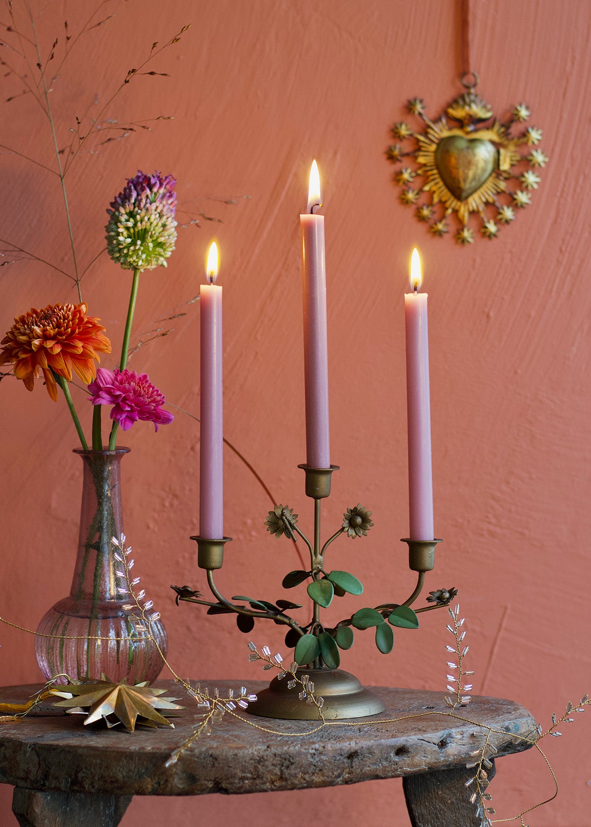 Candle holder with lit candles on a rustic table against a pink wall with decorative elements.