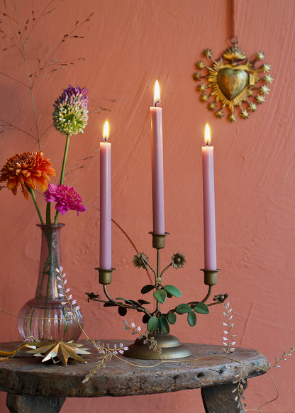 Candle holder with lit candles on a rustic table against a pink wall with decorative elements.