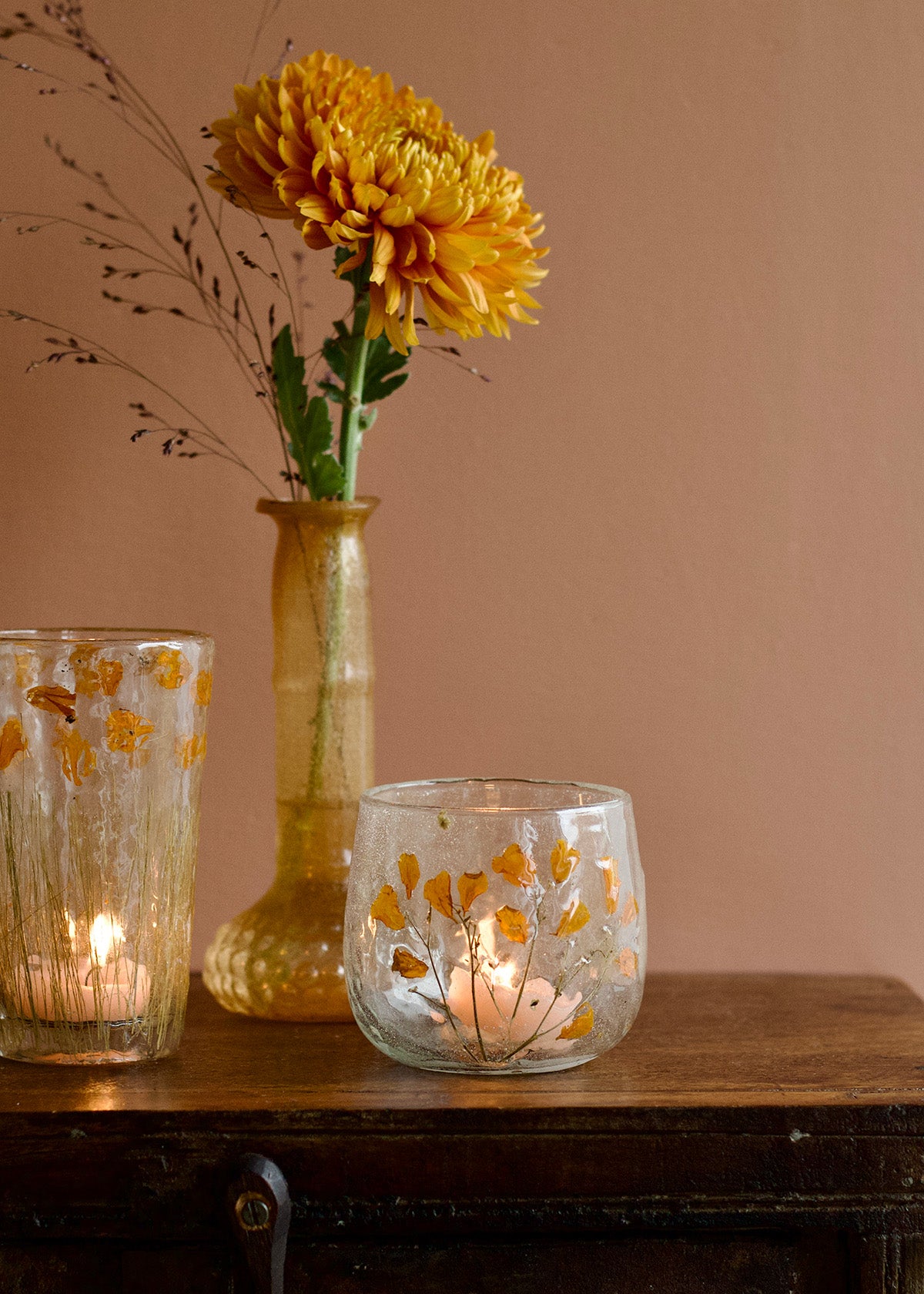 Decorative glass candle holders with floral patterns on a wooden surface against a beige wall.