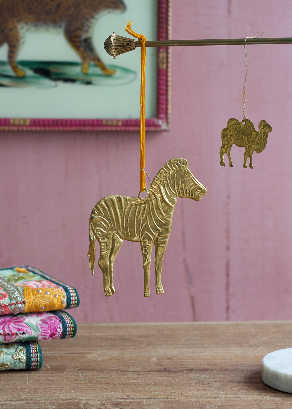 Gold zebra ornament on a wooden surface with a pink wall and framed picture in the background.